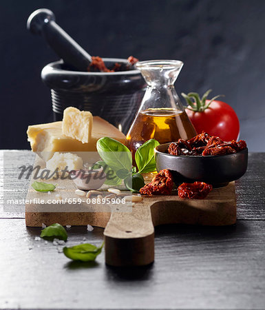 An arrangement of tomatoes, olive oil, parmesan, garlic, pine nuts and basil on a chopping board