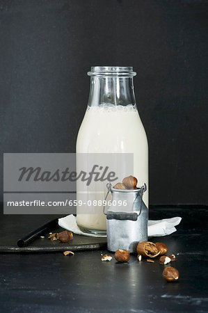 Homemade hazelnut milk in a glass bottle and hazelnuts in a mini milk jug