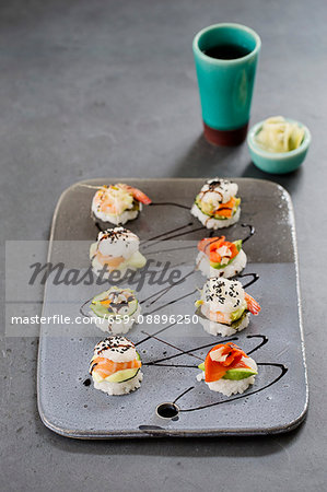 Eight mini sushi burgers on a ceramic plate with smoked and fresh salmon, surimi and shrimp
