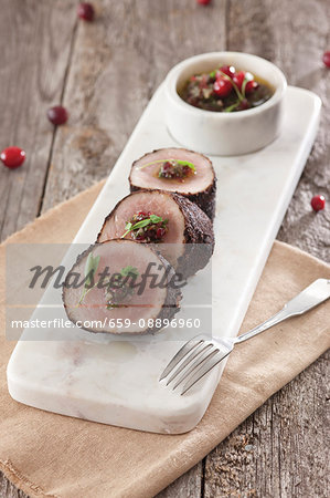 Chili crusted pork tenderloin sliced on white rectanle cutting board with cranberry chimichurri