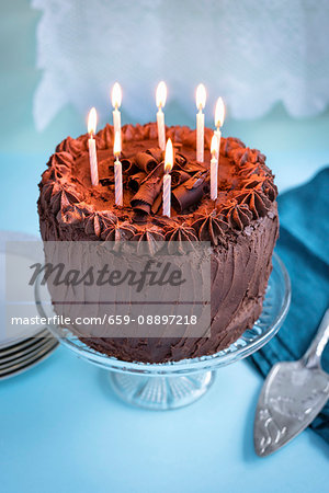 Chocolate birthday cake with 8 lit candles on cake stand