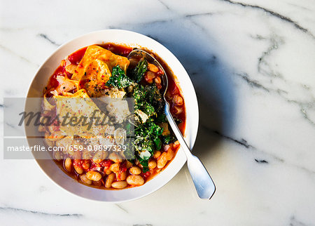 Cannelleni beans with pasta pieces in a tomato based soup topping with kale and cheese