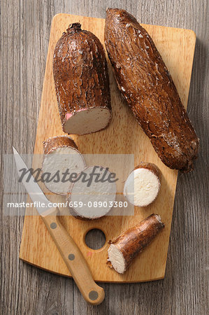 Cassava root, partially sliced, on a chopping board with a knife