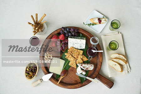 A cheesebaord with fresh fruit, sauces, nuts, capers, breadsticks, crackers and white bread