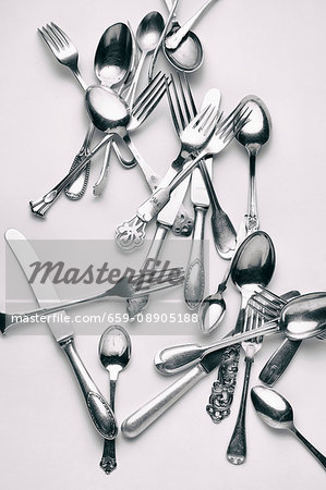 Various forks, knives and spoons on a white surface
