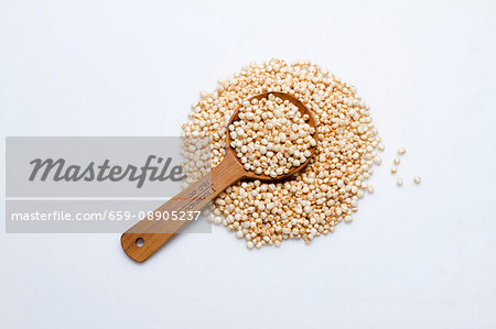 A pile of amaranth flakes with a wooden spoon on a white surface