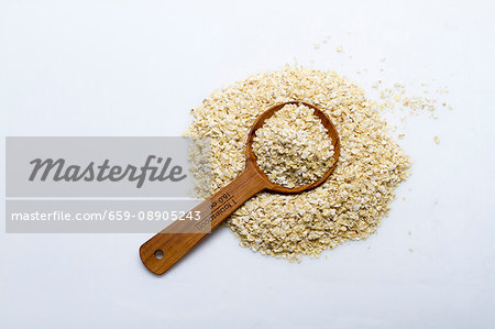 A pile of millet flakes with a wooden spoon on a white surface