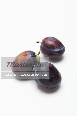 Three damsons on a white surface
