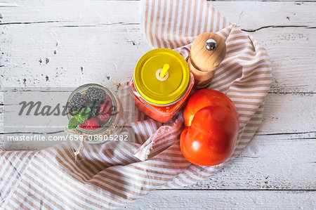 Cold tomato soup in a jar next to muesli with a jar of berries (seen from above)