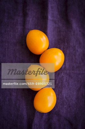 Four yellow tomatoes on a violet cloth