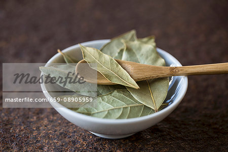 Dried bay leaves with a wooden spoon in a bowl