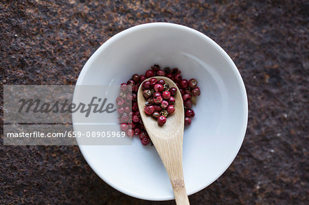 Red peppercorns with a wooden spoon in a bowl (seen from above)
