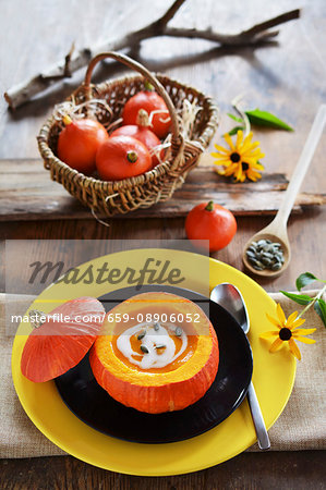 Pumpkin soup served in a hokkaido pumpkin with a basket full of small pumpkins and flowers in the background Pumpkin soup served in a hokkaido pumpkin with a basket full of small pumpkins and flowers in the background