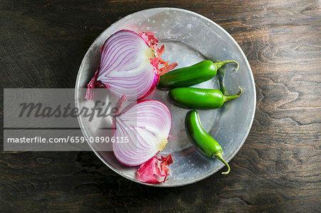 An onion cut in half and chilli peppers on a metal plate