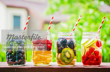 Four fruity drinks in screw-top jars on a garden table