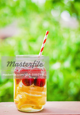 Fruity iced tea in a screw-top jar with a straw on a garden table