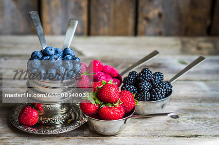 Fresh berries in silver cups on a rustic surface