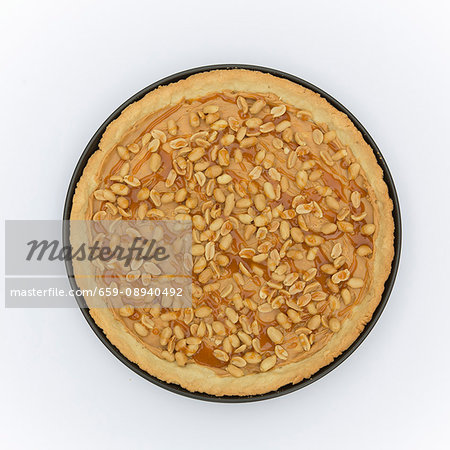 A baked tarte au sucre base in a tart tin with peanut butter, peanuts and caramel sauce