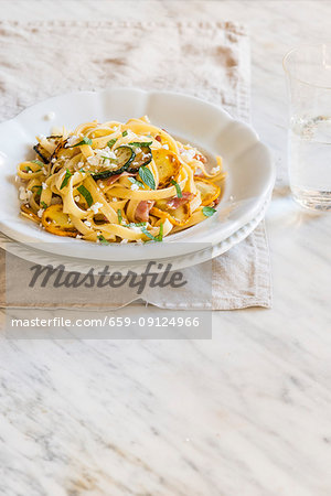 Fresh homamade tagliatelle with yellow and green courgette, bacon and goat cheese