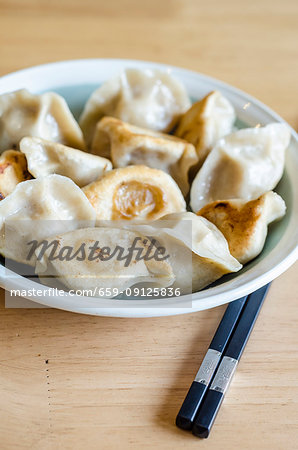 Bowl of grilled dchinese dumplings with chopsticks on a wooden table