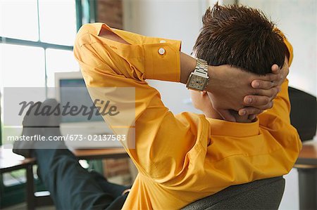 A man leaning back at his desk and thinking.