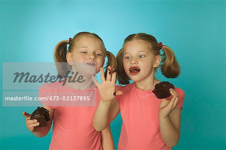 Twin girls eating chocolate cake.