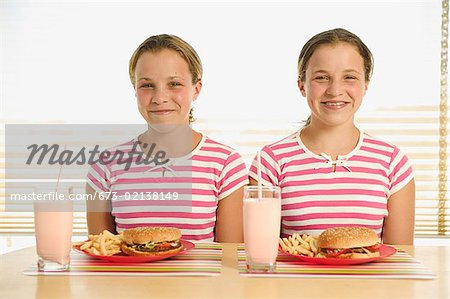 Twin teenagers with hamburgers, french fries, and milkshakes.