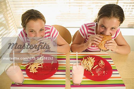 Twin teenage girls eating hamburgers.