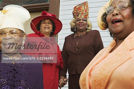 Four senior women wearing hats and singing on church steps.