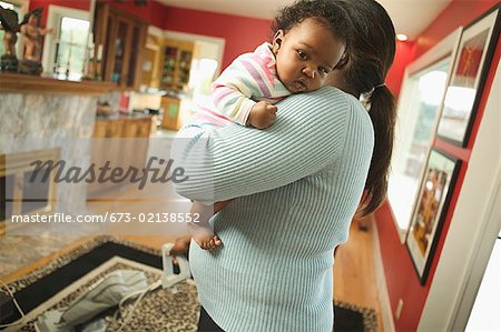 Woman holds baby while vacuuming.