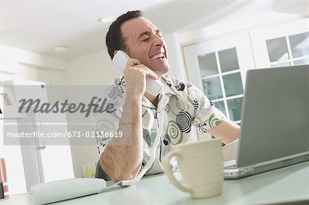 Man talking on the phone and working on a laptop.