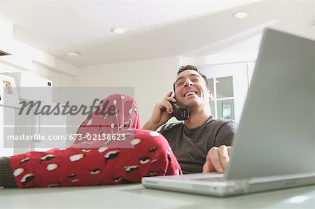 Man in pajamas talking and working on a laptop.
