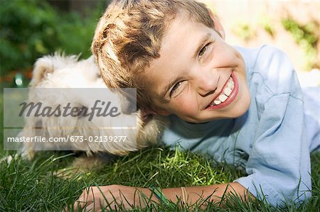 Boy and dog lying down together outdoors