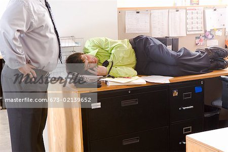 Boss Discovering Employee Asleep On Desk Stock Photo
