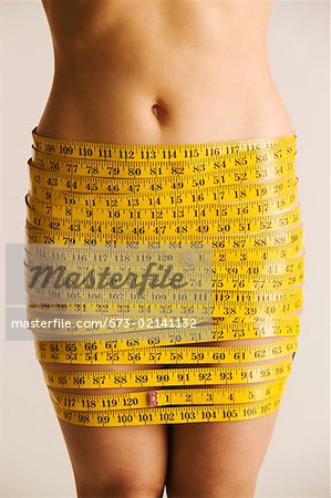 Midsection of nude woman wrapped in measuring tape