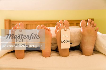 Couple s bare feet with Do Not Disturb Til Noon signs Stock Photo