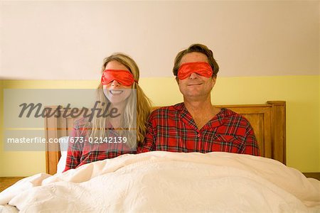 Couple sitting in bed wearing eye masks