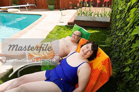 Couple relaxing on lawn chairs in backyard Stock Photo