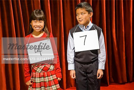 Asian girl and boy wearing numbers on stage