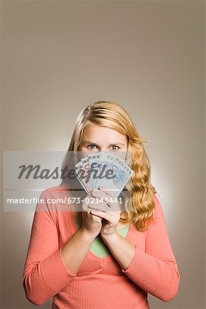 Teenage girl holding money in front of face