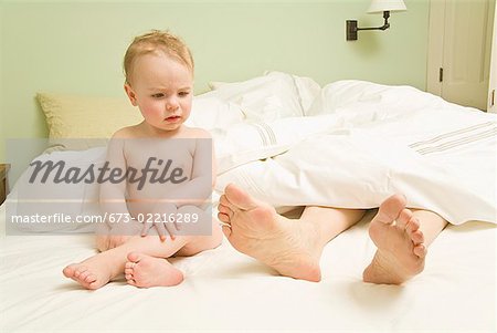Curious baby looking at mother’s feet in bed