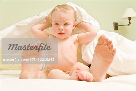 Sad baby and mother’s feet under blanket in bed