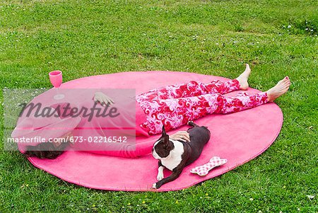 Woman in pink and dog relaxing outdoors on rug