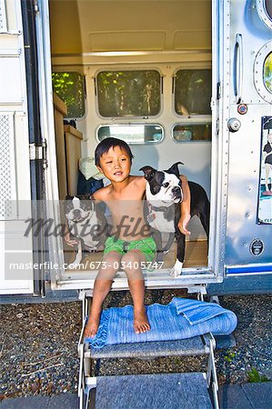 Boy sitting in door of camper with dogs
