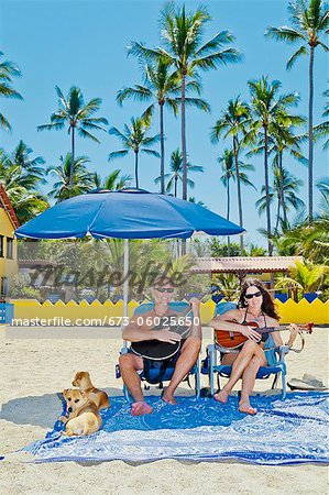 Happy man and woman in beach chairs with guitars and dogs