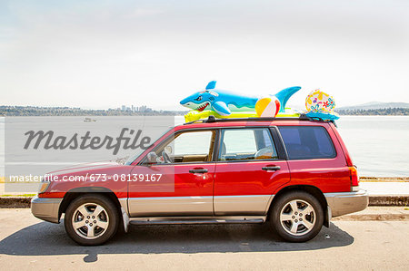 Car with beach toys and floaties on the roof parked by a lake