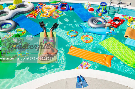 Man wearing flippers floats in a pool full of inflatable toys Man wearing flippers floats in a pool full of inflatable toys