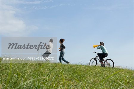 Young woman riding bicycle behind two young men running
