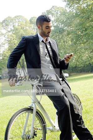 Businessman with bicycle and cell phone in park
