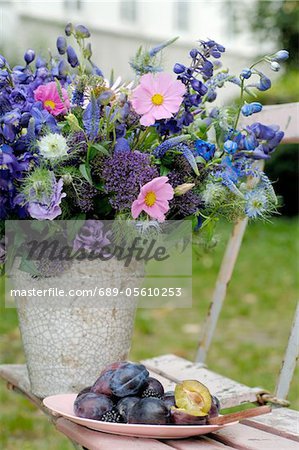 Bunch of summer flowers and plums on garden chair